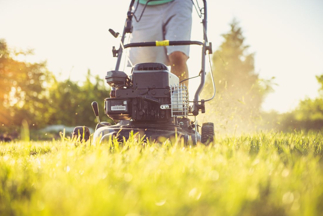 Hands guiding a mower across a healthy lawn